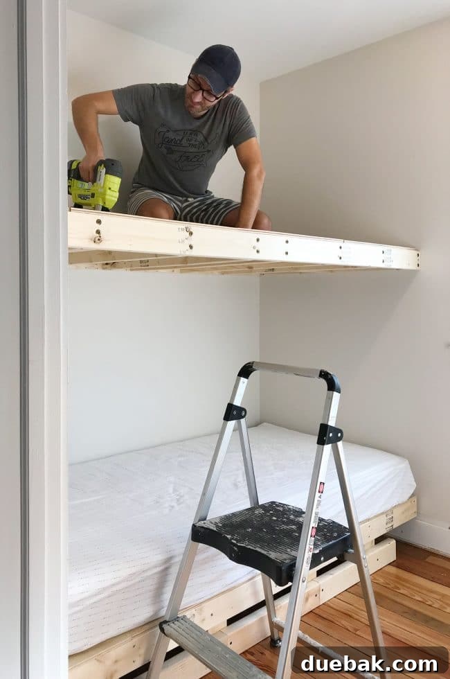 Constructing Bespoke Bunk Beds 17 John sitting on the newly constructed top bunk to securely nail plywood panels into the floating platform, testing its sturdiness.