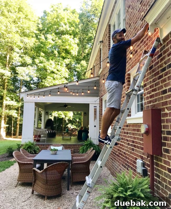 Out With the Deck, In With a Pea Gravel Patio 17 One person attaching garden string lights to an anchor point on the house siding.