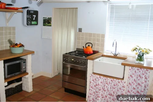 Cottage Chic White Kitchen with Belfast Sink Cozy and rustic English cottage kitchen featuring white cabinetry, solid oak countertops, a classic Belfast sink, and a vibrant orange Le Creuset kettle.