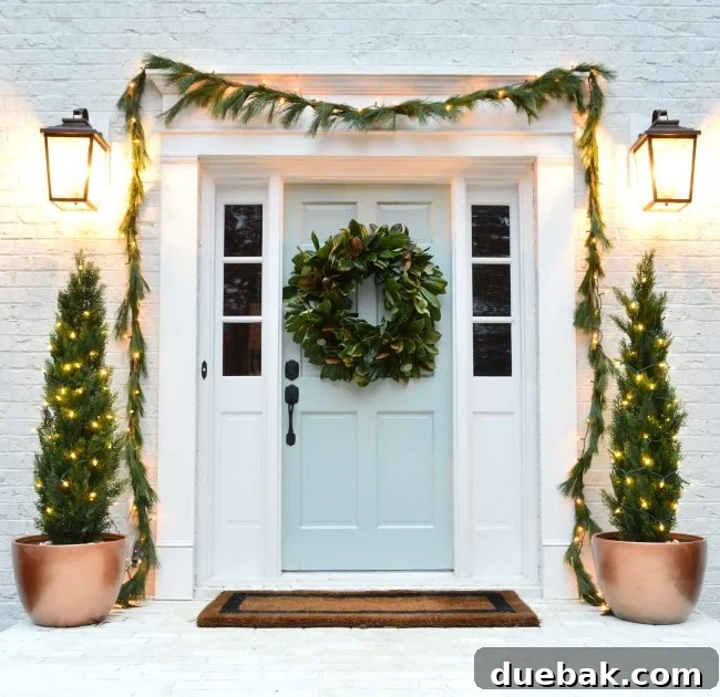 Double the Sparkle: Holiday Decorating at Home and the Beach 2 A festive white brick house exterior decorated with warm white LED lights on trees and garlands around the door.