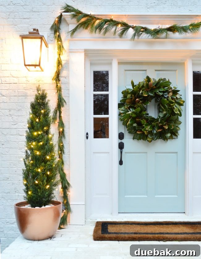 Double the Sparkle: Holiday Decorating at Home and the Beach 3 A close-up of a front door decorated with a magnolia wreath and fresh evergreen garlands with warm white lights.
