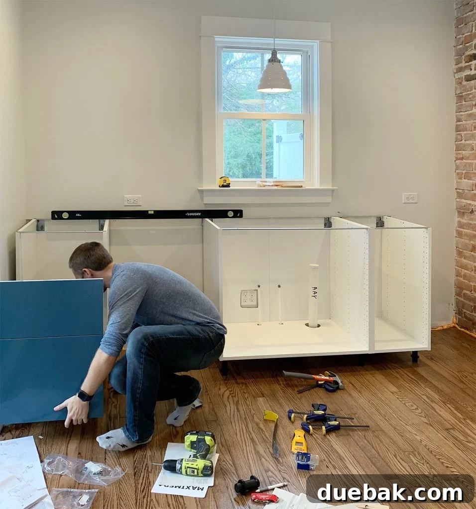 A partially installed Ikea kitchen cabinet system, showing the metal rail and shims used to straighten a bowed wall.