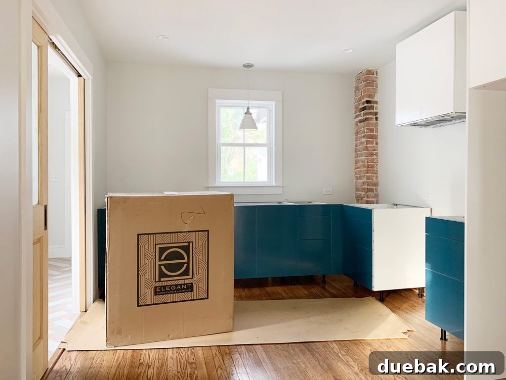 Left side duplex kitchen with moody blue-green-gray cabinets (with protective film) and pendant light.