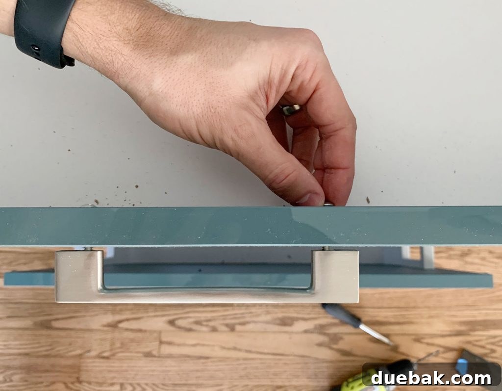Tightening Kitchen Cabinet Hardware Screw By Hand, ensuring a snug fit without over-tightening.