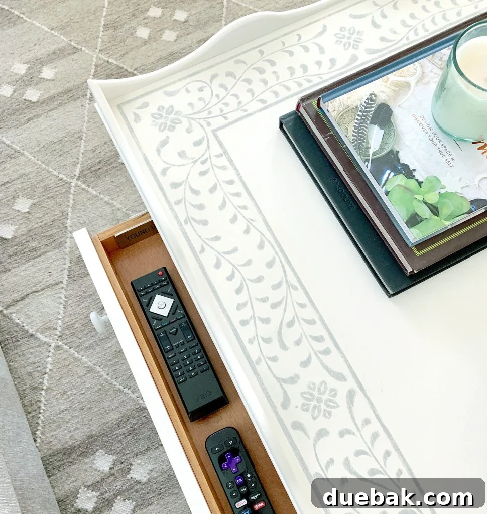 Small remote drawer open on the scalloped coffee table with a stencil inlay pattern, revealing hidden storage.