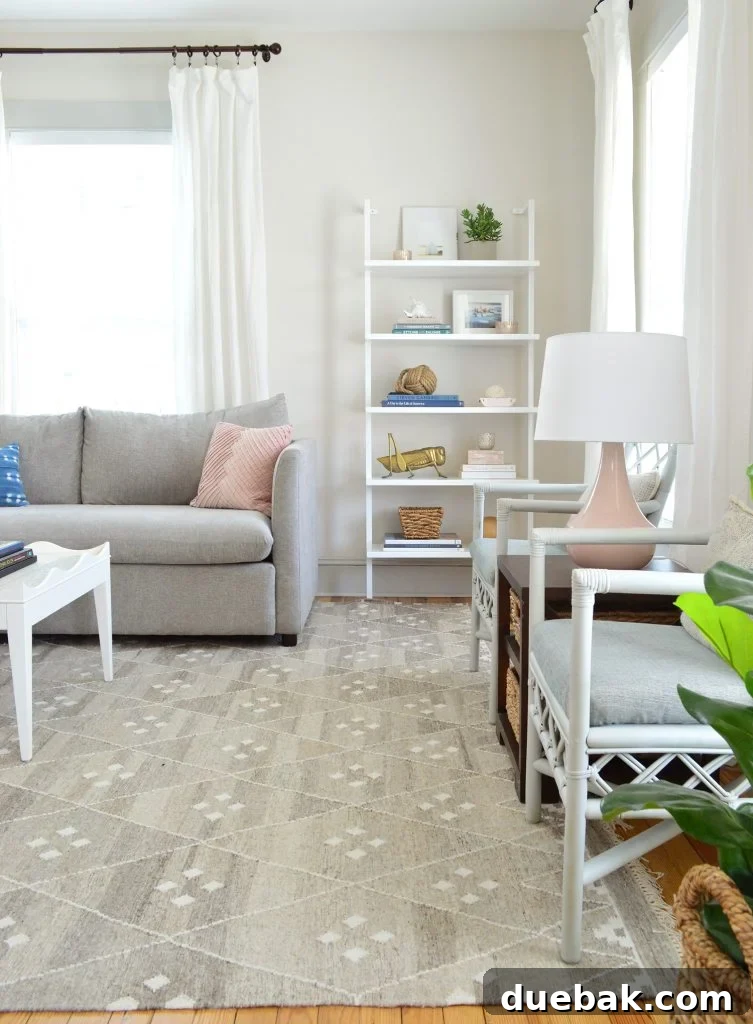 Tall CB2 bookcase in a neutral gray living room with pink lamps and accessories, adding vertical interest and personal touches.