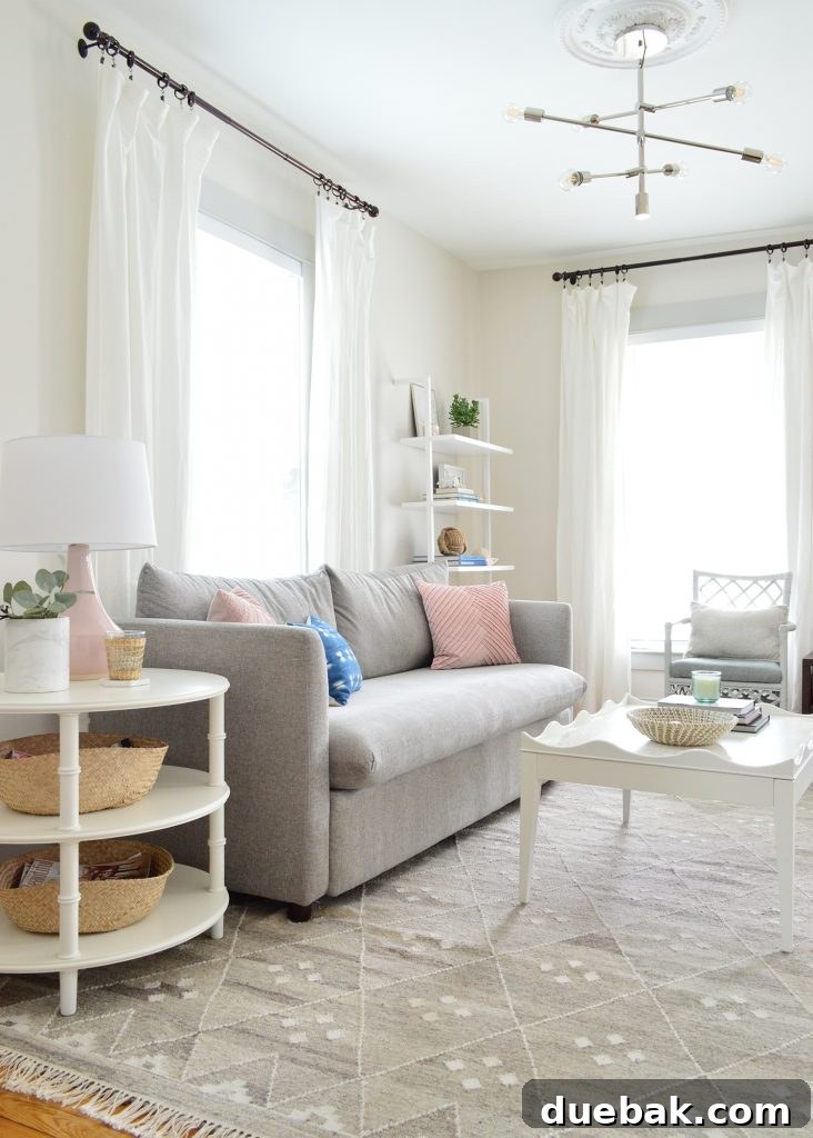 Bright neutral living room featuring the new gray performance fabric sofa with a round side table and the scalloped coffee table, enhancing the light and airy feel.