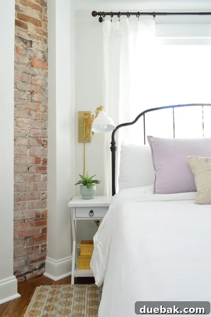 Our Airbnb Bedroom and Bathroom Makeover Full Reveal 4 Close-up of the main bedroom showcasing the metal bed, crisp white bedding, and wall-mounted accordion sconces against a serene backdrop.