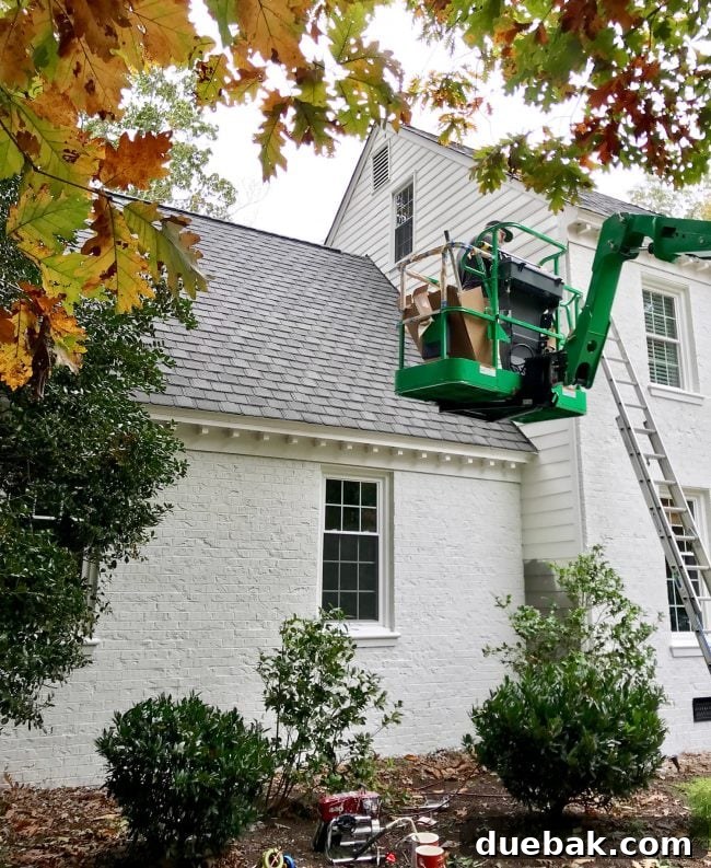 Painter in a crane painting the siding of a brick house white