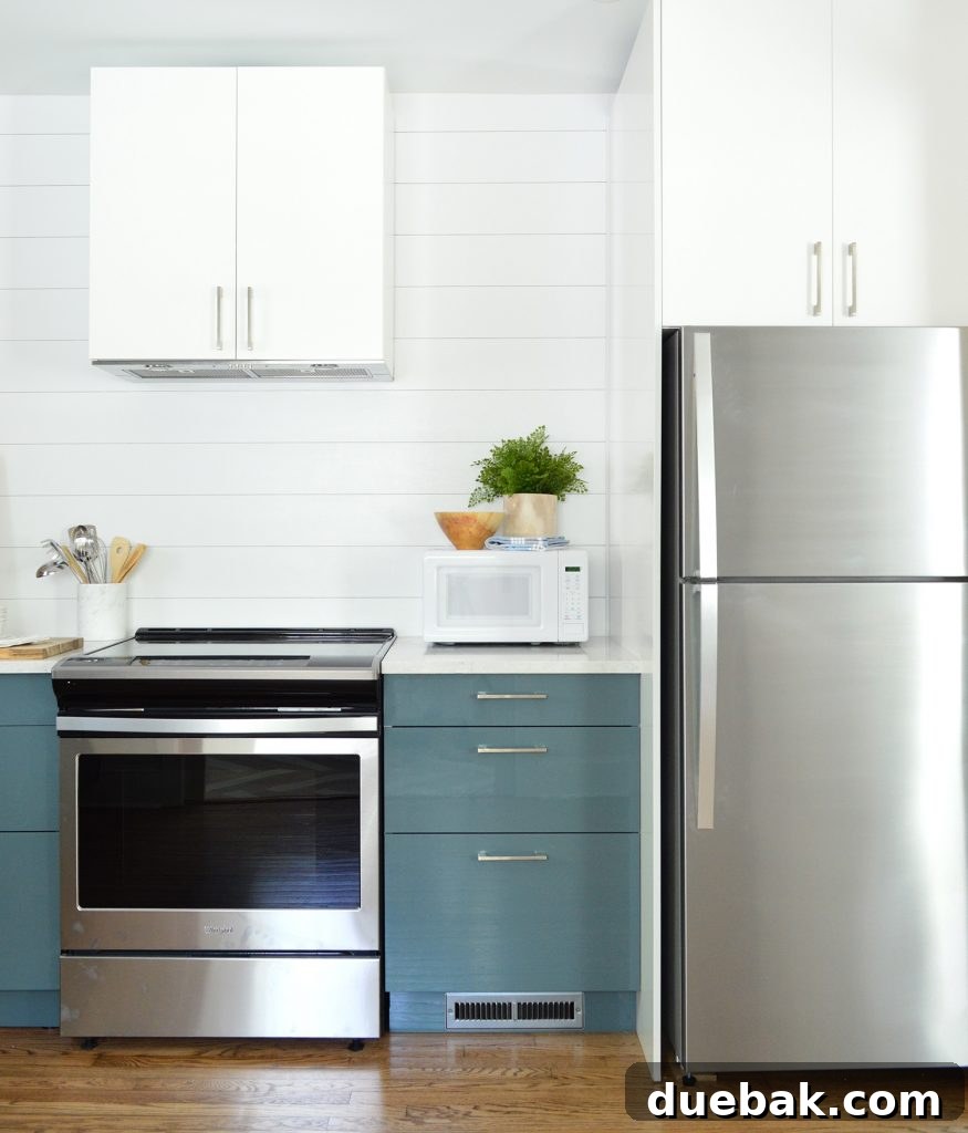 Dual Kitchen Transformations: Our Airbnb's Story 12 White planked shiplap wall paired with blue Ikea cabinets, featuring integrated appliances for a modern kitchen look.