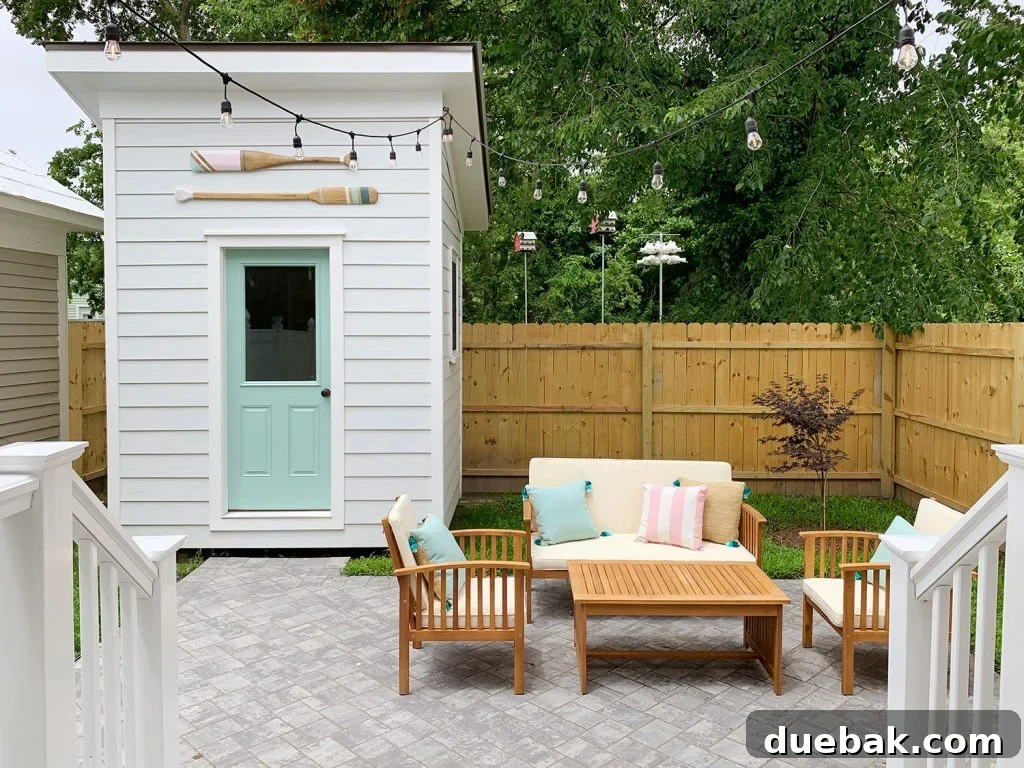 View of the left side backyard from the back door, featuring comfortable outdoor furniture, ambient string lights, and decorative oars on the shed.