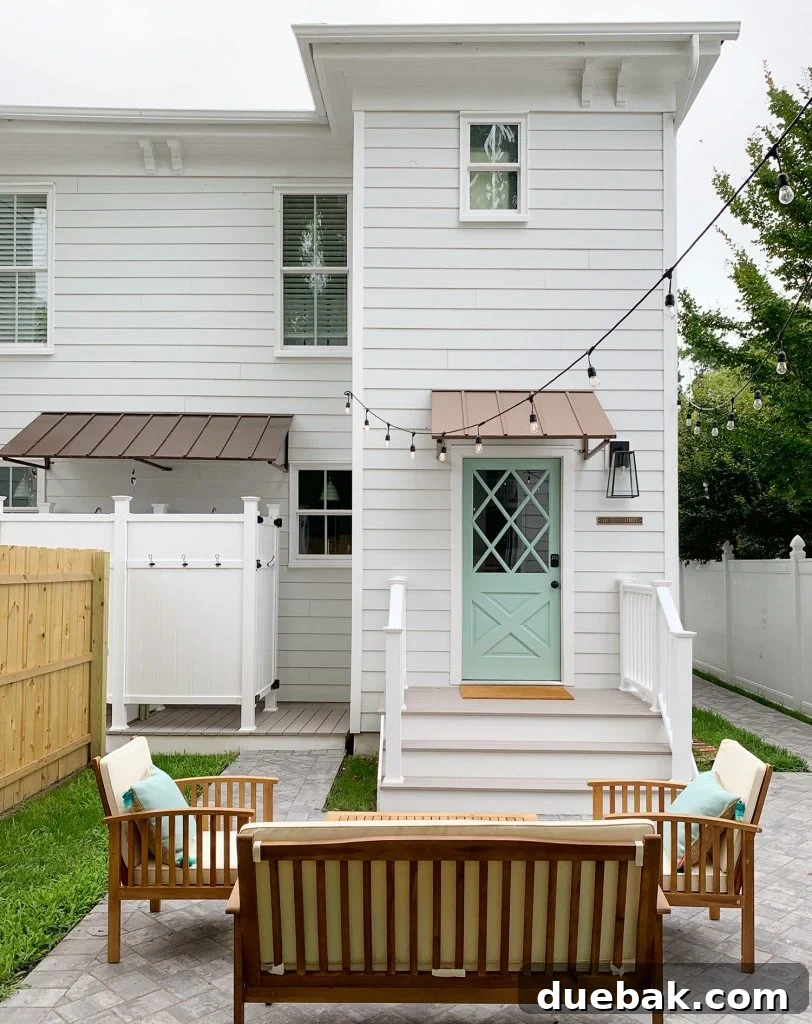 Back door view of the left duplex unit with an address plaque, keypad lock, and porch lantern, framed by crepe myrtles along the fence.