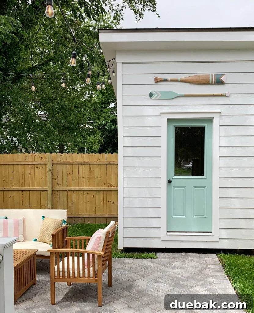Close-up of the duplex backyard shed with custom-painted decorative oars, comfortable outdoor furniture, and striped pillows, all complemented by a door in Pale Patina.