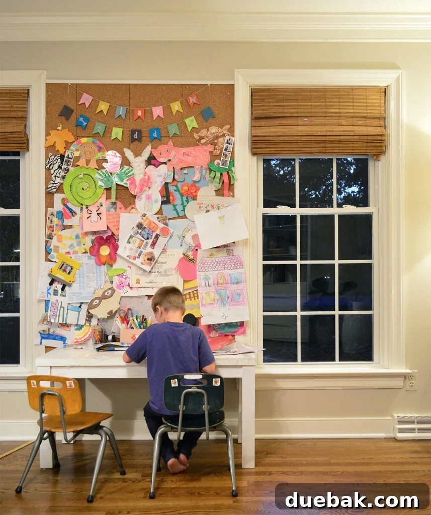 A large corkboard covered with children's colorful 2D artwork and drawings, proudly displayed in an office.