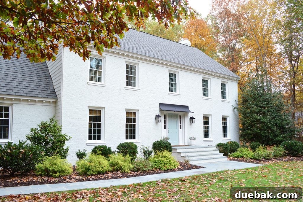 Detail shot of the white painted brick house with the newly installed, elegant awning, surrounded by fall foliage.