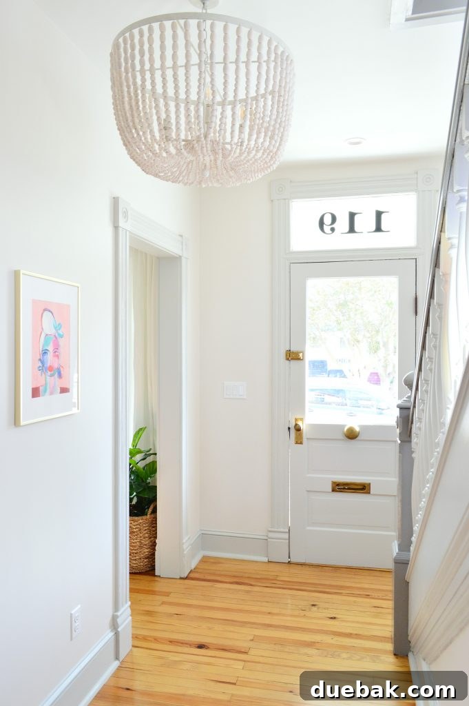 7 Beach House Renovations and the Story Behind Each Space 5 Elegant white beaded chandelier in a bright beach house foyer with a glass-front door and colorful art