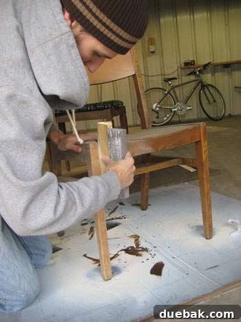 Close-up of a vintage wooden chair being sanded with 100-grit sandpaper, revealing the raw wood beneath the old finish.