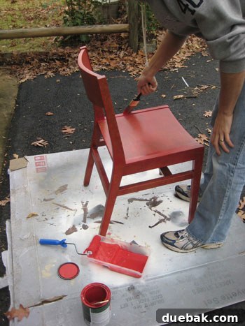 Vintage wooden chair being painted with a vibrant semi-gloss red latex paint, showing careful brush application.