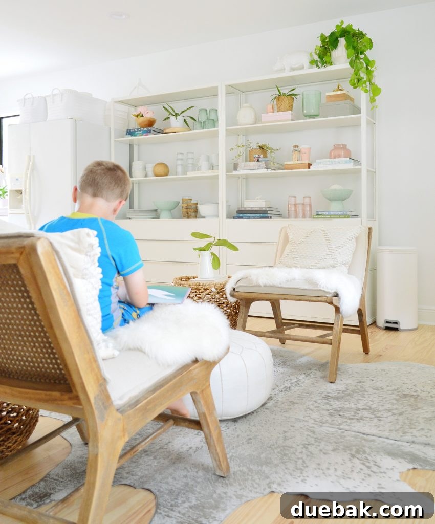 Compact Kitchen Living: Three Weeks In 15 A cozy sitting nook with two light-colored chairs and a textured pouf on a patterned rug. A tall plant and white bookshelf are visible in the background, creating an inviting space.