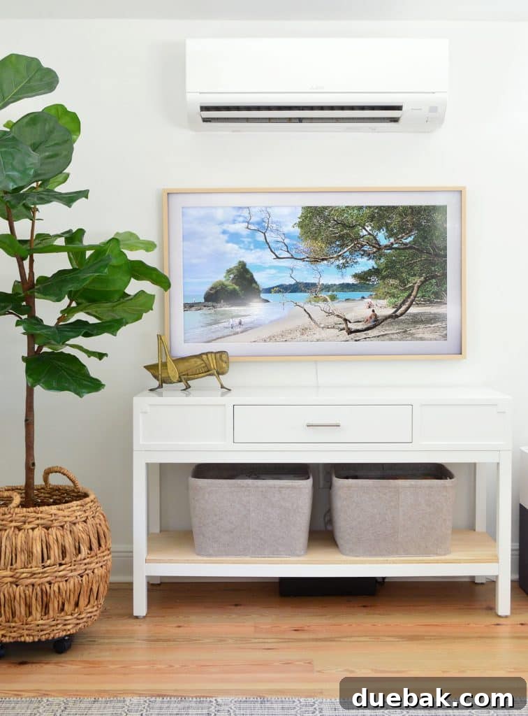 Life in Our Upstairs Family Room Four Weeks In 9 Detail shot of the Samsung Frame TV displaying art, positioned below a white mini-split unit and beside a tall faux fig tree. Felt storage baskets are visible on the console, contributing to a clean and functional design.