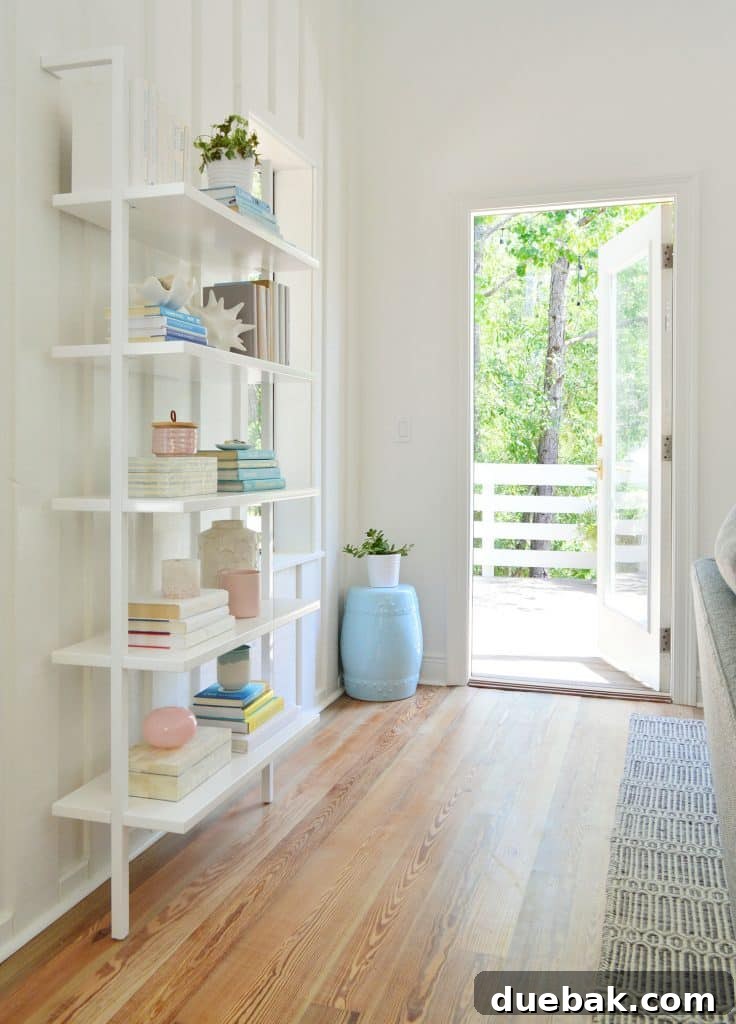 Life in Our Upstairs Family Room Four Weeks In 11 Floating white wall bookcase next to an open door leading to the outdoor deck, showcasing efficient space utilization in a bright beach house interior.