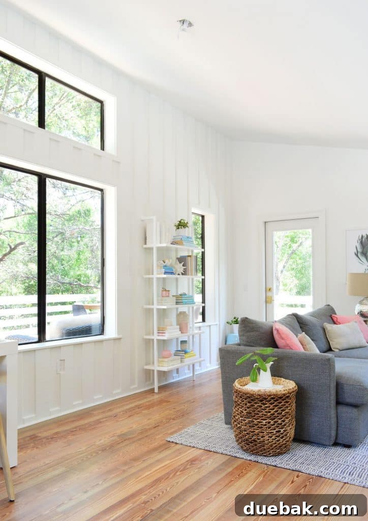 Life in Our Upstairs Family Room Four Weeks In 12 Bright beachy living room showcasing a large window, a cozy sofa, and a wall bookcase, with an empty ceiling junction box awaiting a new light fixture, highlighting future design plans.