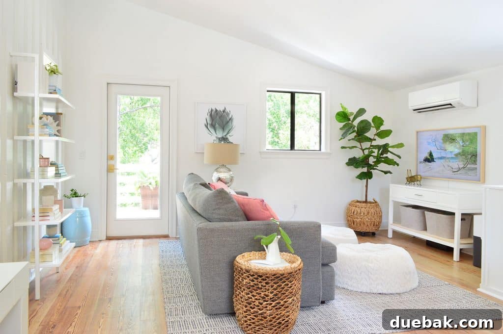 Life in Our Upstairs Family Room Four Weeks In 3 Bright beachy living room featuring a comfortable gray sofa facing a wall-mounted television, with a large window to the left and a wall bookcase, all bathed in natural light.