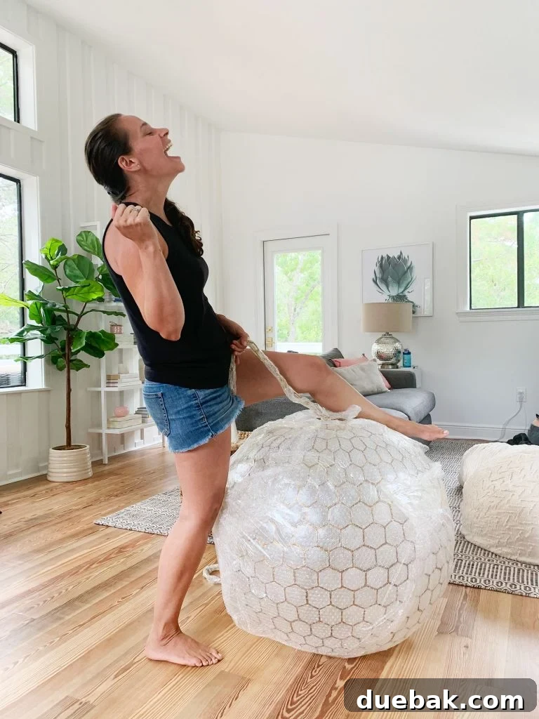 Installing Serena & Lily's Statement Chandelier 4 Sherry Pretending To Reenact Miley Cyrus Wrecking Ball On Large Capiz Globe Light, providing a humorous perspective on the chandelier's size.