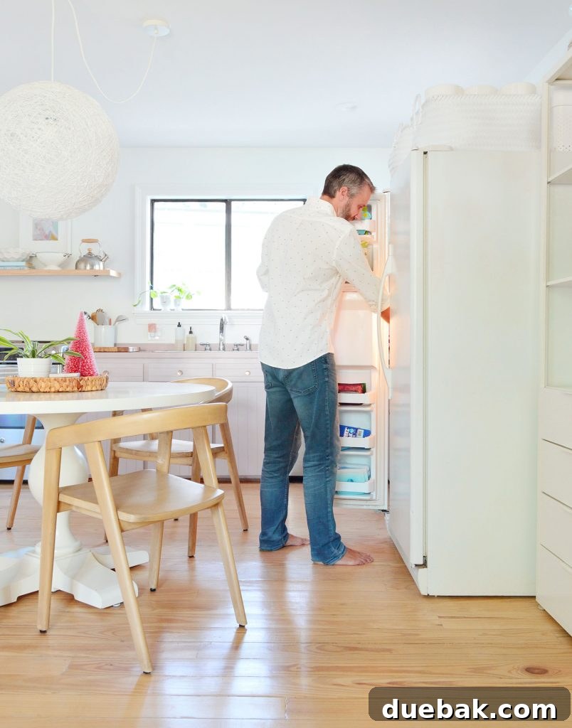 John standing with the freezer door open next to the round dining table in the kitchen, demonstrating access
