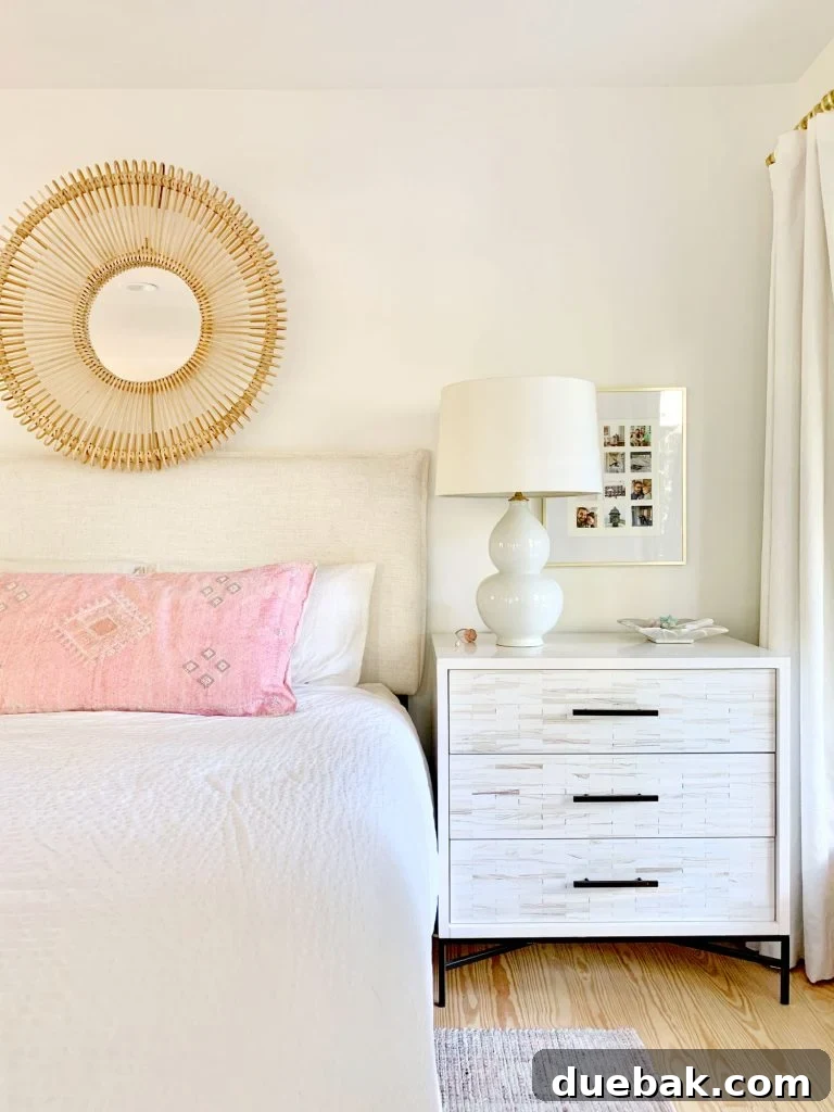 Linen headboard on bed with white bedding and inlay dresser as nightstand