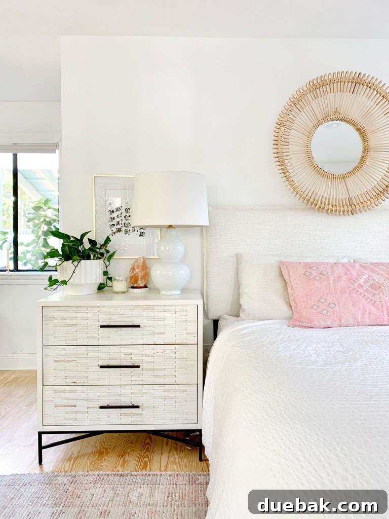 Linen headboard on bed with white bedding and inlay dresser as nightstand