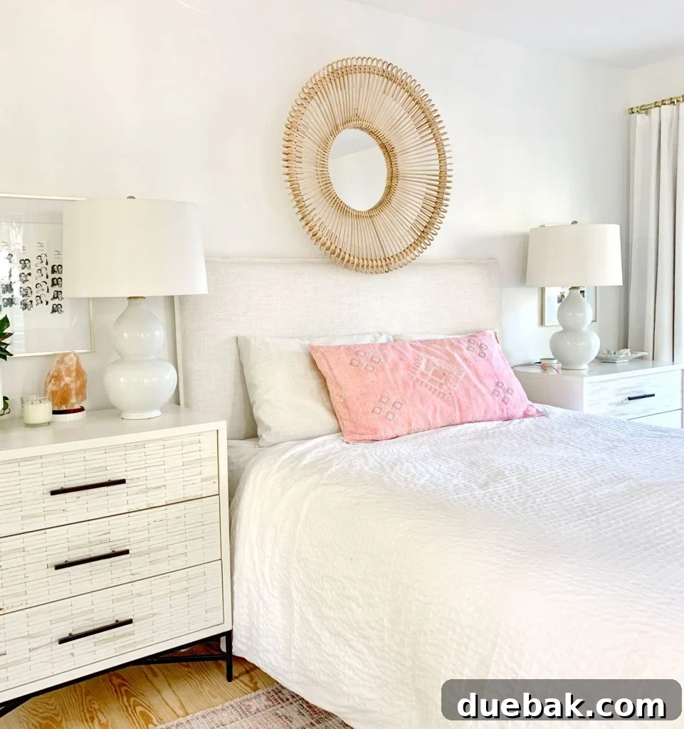 Linen headboard on bed with white bedding and round wicker mirror over headboard
