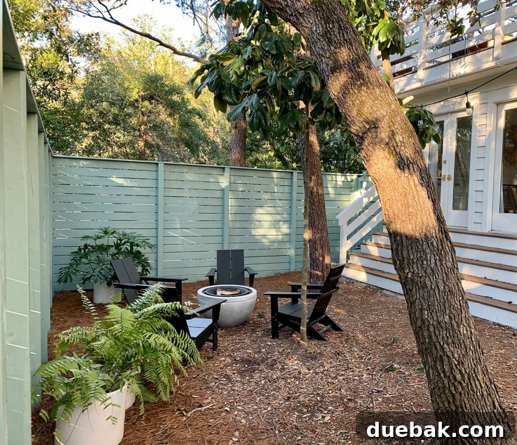 Green fenced side yard with black Adirondack chairs around fire pit