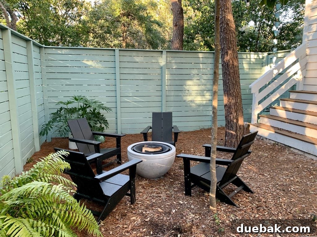 Painted fenced side yard with black Adirondack chairs around fire pit with potted plants