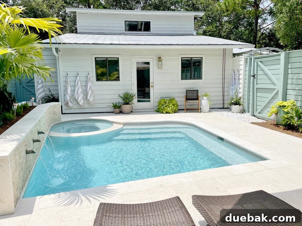 Small freeform pool with white house metal roof in background, showing a perfectly designed aquatic retreat.