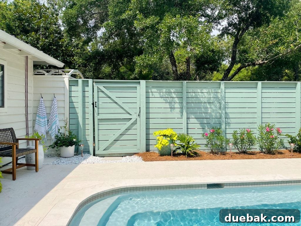 Pool fence with horizontal slats and gray green paint with planting bed in front, blending natural elements.
