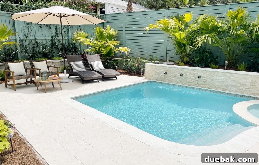 Small freeform pool enclosed by green fences with DiamondBrite Ivory plaster and shellstone travertine, creating a secluded retreat.