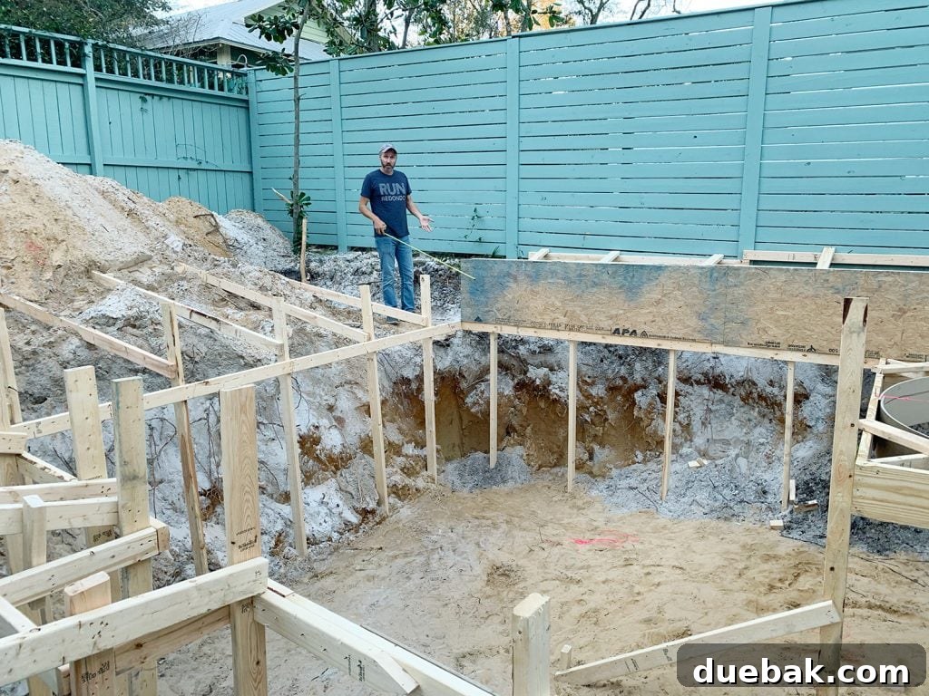 John standing next to frame pool hole during backyard Florida pool construction, showing the sandy soil.
