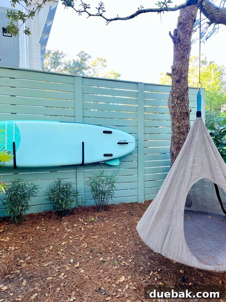 The organized side yard area, featuring a paddleboard cleverly stored on the fence alongside the hanging tent swing