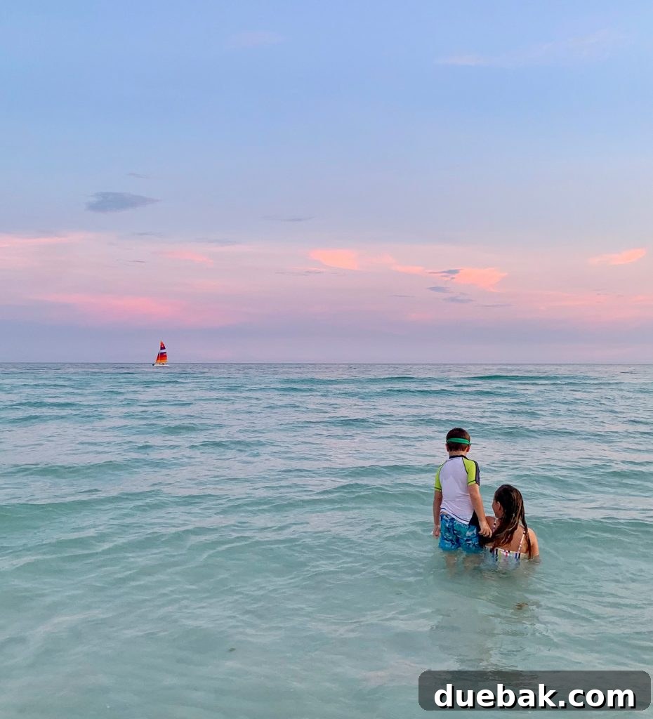 Kids playing in Gulf of Mexico at sunset with sailboat in background